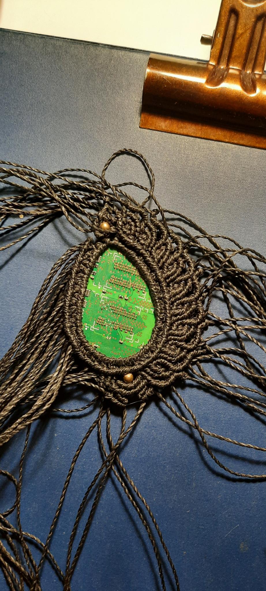 pendentif flamme en fils noirs sertissant un morceau de circuit imprimé vert en forme de goutte. Bijou en cours de création